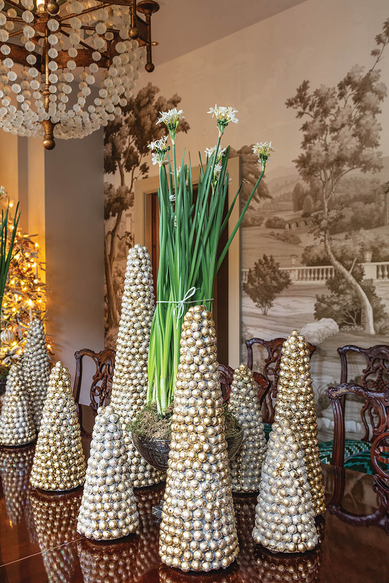 It’s all about layering: For the dining room’s winter wonderland, John adds dimension and volume to each tree and strand of garland through abundant candles, ornaments, and ribbon. But he also considers how complementary design elements—here, a collection of metallic tabletop trees, elegant potted paper-whites, and fluffy faux snow—will fully bring the space to life. After all, more is more during the holiday season.