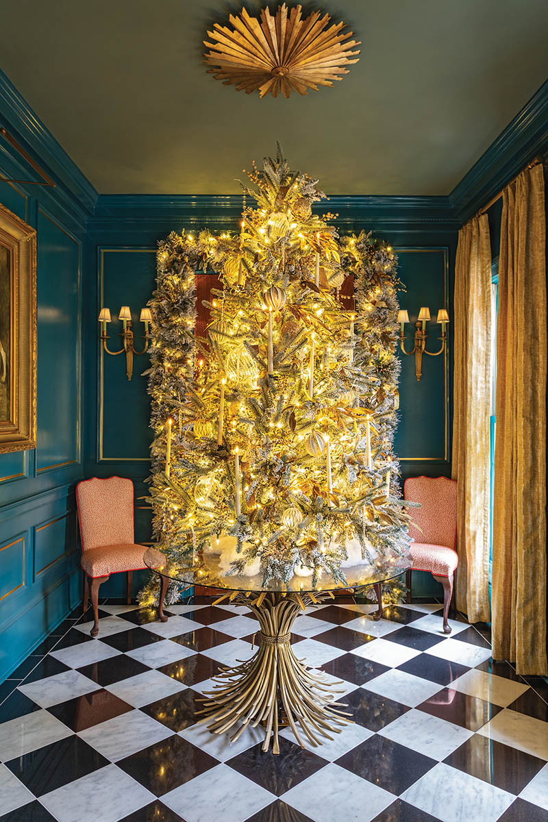 Upon entry, guests pass beneath garland and are greeted with a petite flocked tree adorned with candles and elegant glass and gilded ornaments, all aglow against the foyer’s walls painted in Sherwin-Williams “Port Royal” from the Colors of Historic Charleston collection.