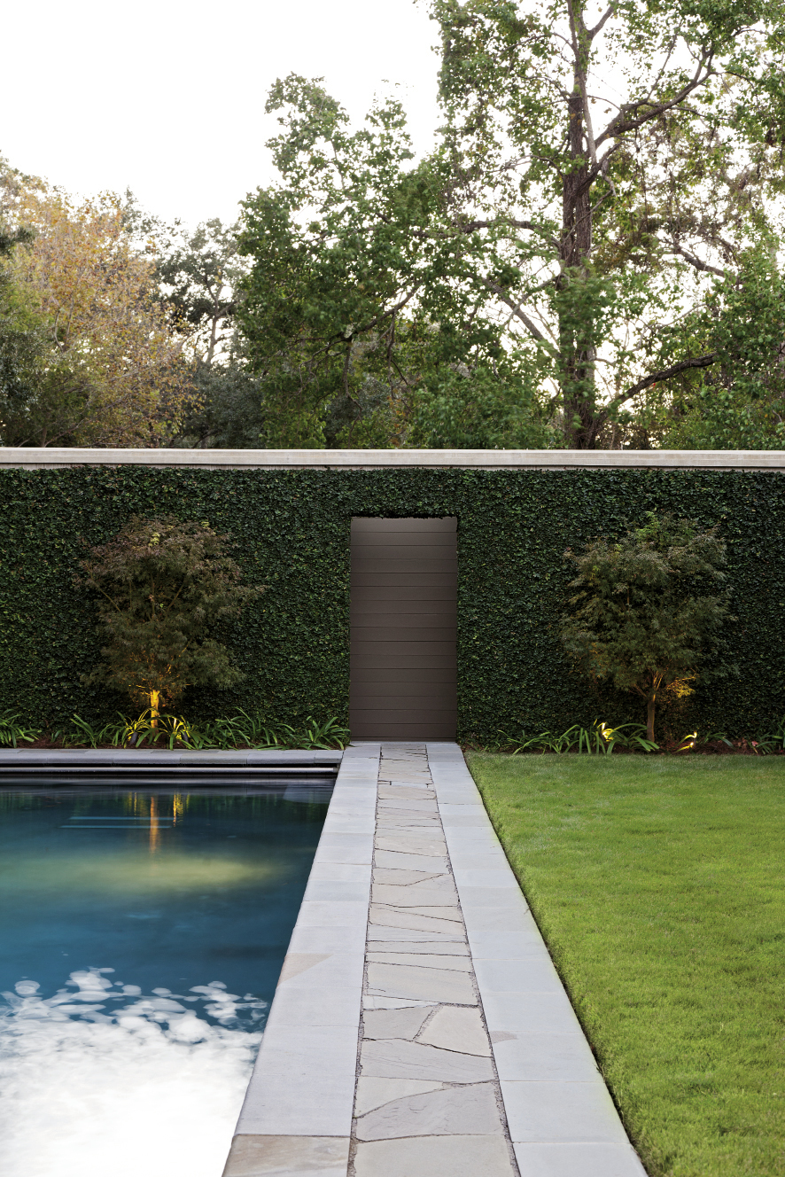 Green-leaf Japanese maples flank a door on the back garden wall, while a metal alligator adds a touch of poolside humor.
