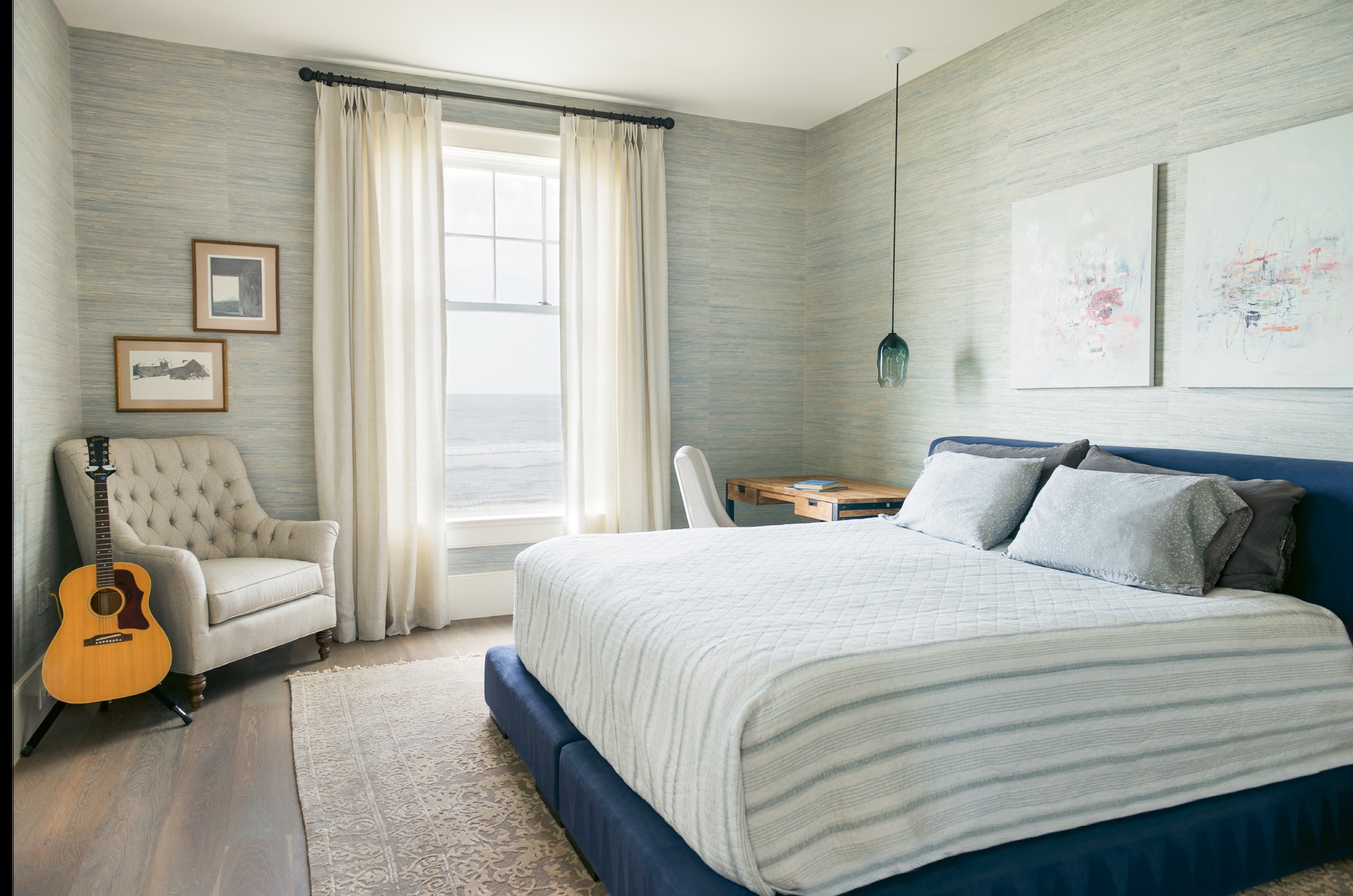 In the master bedroom, modern touches, such as paintings by Tim Hussey, commingle with traditional pieces, like a tufted club chair.