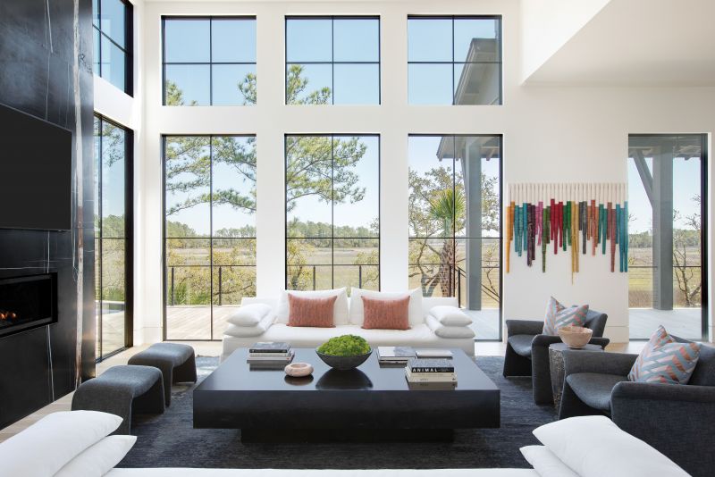 YIN &amp; YANG: Erickson helped her clients move from a more transitional style in their previous home to the bold look they were craving. She pulled the Sherwin Williams “Iron Ore” paint from the exterior into the main living space, anchoring it with a striking book-matched, honed Nero Dorato marble fireplace surround. Dark furniture—Verellen chairs in a bouclé fabric and a wood coffee table designed by Erickson—are balanced by soft white sofas and walls painted with Benjamin Moore’s “Decorator’s White.” The designer also pulled hues from the marble and tied them into custom art pieces that pop from the neutral backdrop.