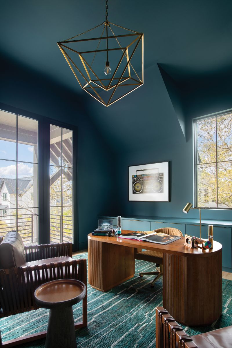 Office Space: The upstairs study’s warm wood furniture, topped by a chandelier from Visual Comfort, stands out against the rich blue-green walls painted in C2 “Titan.” The mid-century modern desk is from CB2; its Mad Men vibes are echoed in the leather “Commodore” chairs from Palecek. A green Moroccan rug from Moattar in Atlanta ties it all together. The consoles, painted the same colors as the walls, expertly blend in, allowing the photography from Heart of Gold Gallery in Mount Pleasant to sing.