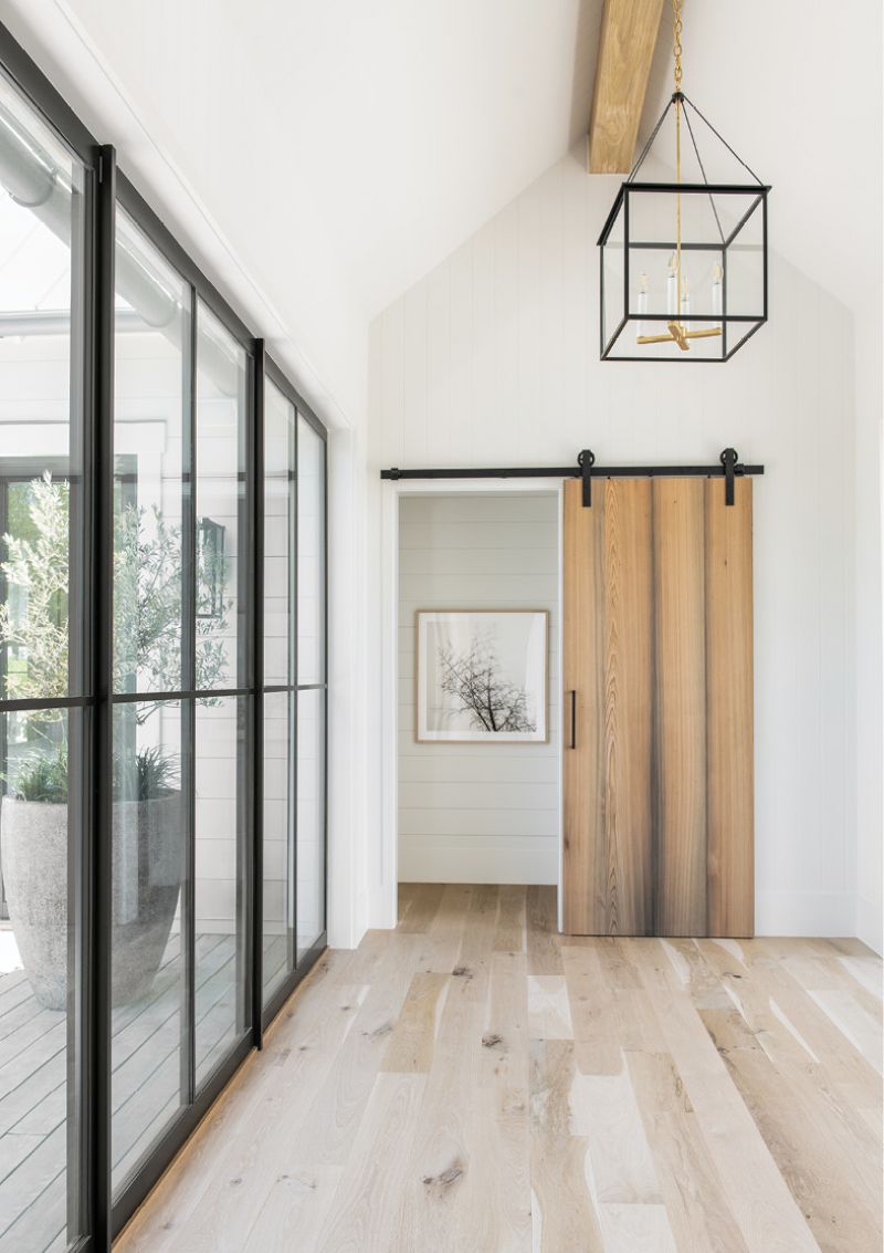 Feature &amp; Function: Designed to draw the eye to the landscape beyond its floor-to-ceiling windows, the entryway’s white oak flooring, cypress barn door, and wooden beam are accented by steel and glass, including an Urban Electric light fixture and custom door hardware.