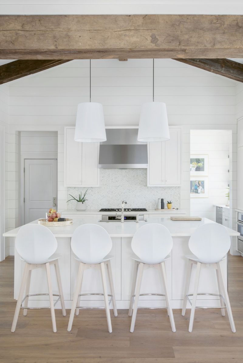 In the streamlined kitchen, seamless cabinetry on each side of the expansive marble-topped island holds everything from cookware to craft supplies, as well as a built-in beverage cooler for kids’ drinks. To the right of the chevron-tiled backsplash, a walk-in pantry houses cooking staples and the wine bar.