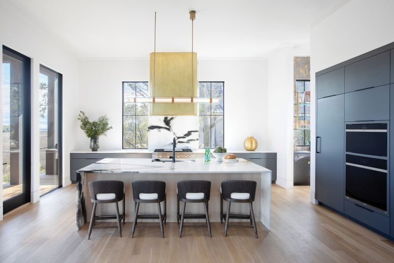 The Open Kitchen continues the color story with the same exterior black on the cabinetry, offset by a stunning black-and-white “Orca” marble countertop and backsplash. The brass-paneled hood, made by local craftsman Matt Burchette, provides a statement piece balancing the marble fireplace on the far side of the room.