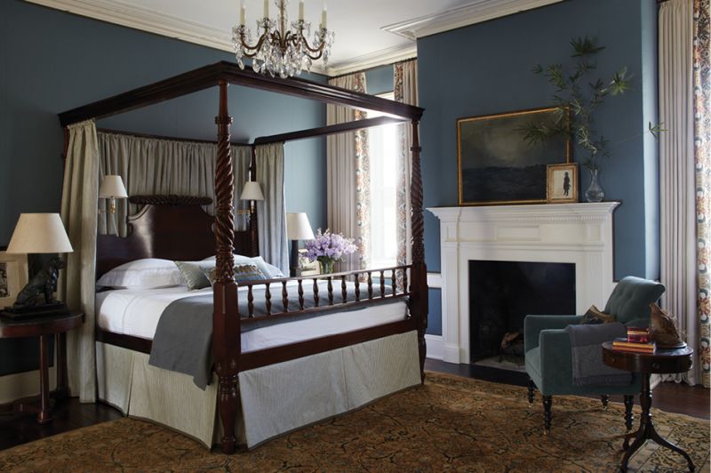 In the primary bedroom, a stunning St. Thomas Regency four-poster bed, sourced from David Skinner Antiques, rests on a wool rug from Iran, circa 1900. Linen drapes from Chelsea Editions bordered with a palm tree pattern brighten the handsome space.